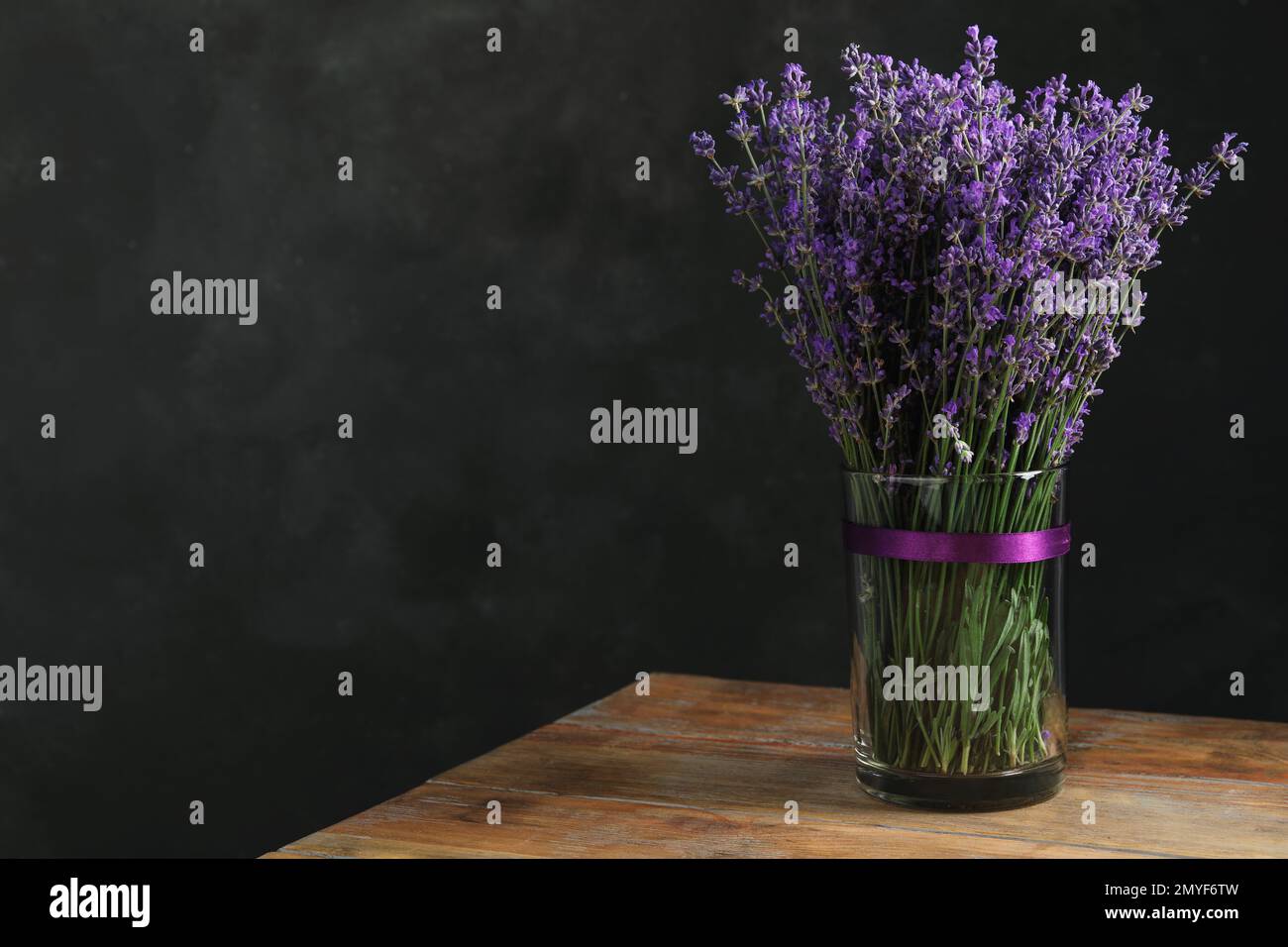 Wunderschöne Lavendelblumen in Glasvase auf Holztisch vor dunklem Hintergrund. Platz für Text Stockfoto