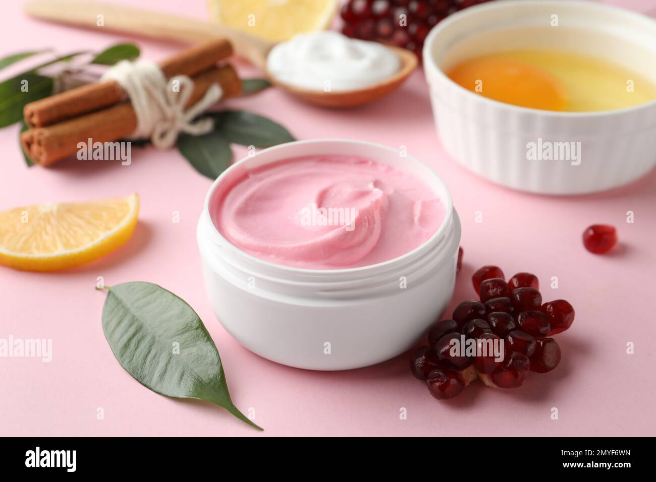 Frischer Granatapfel und Glas Gesichtsmaske auf rosa Hintergrund. Natürliche organische Kosmetika Stockfoto