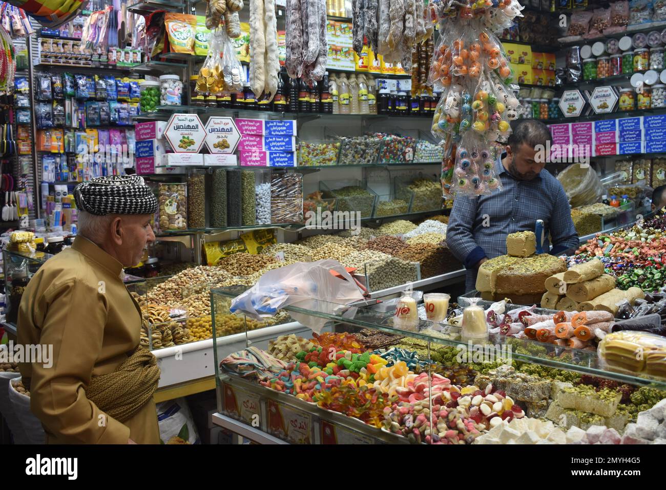 Ein Mann in traditioneller kurdischer Kleidung, der Süßigkeiten im Süßwarenladen im Souk (Markt), Duhok, Nordirak kauft Stockfoto