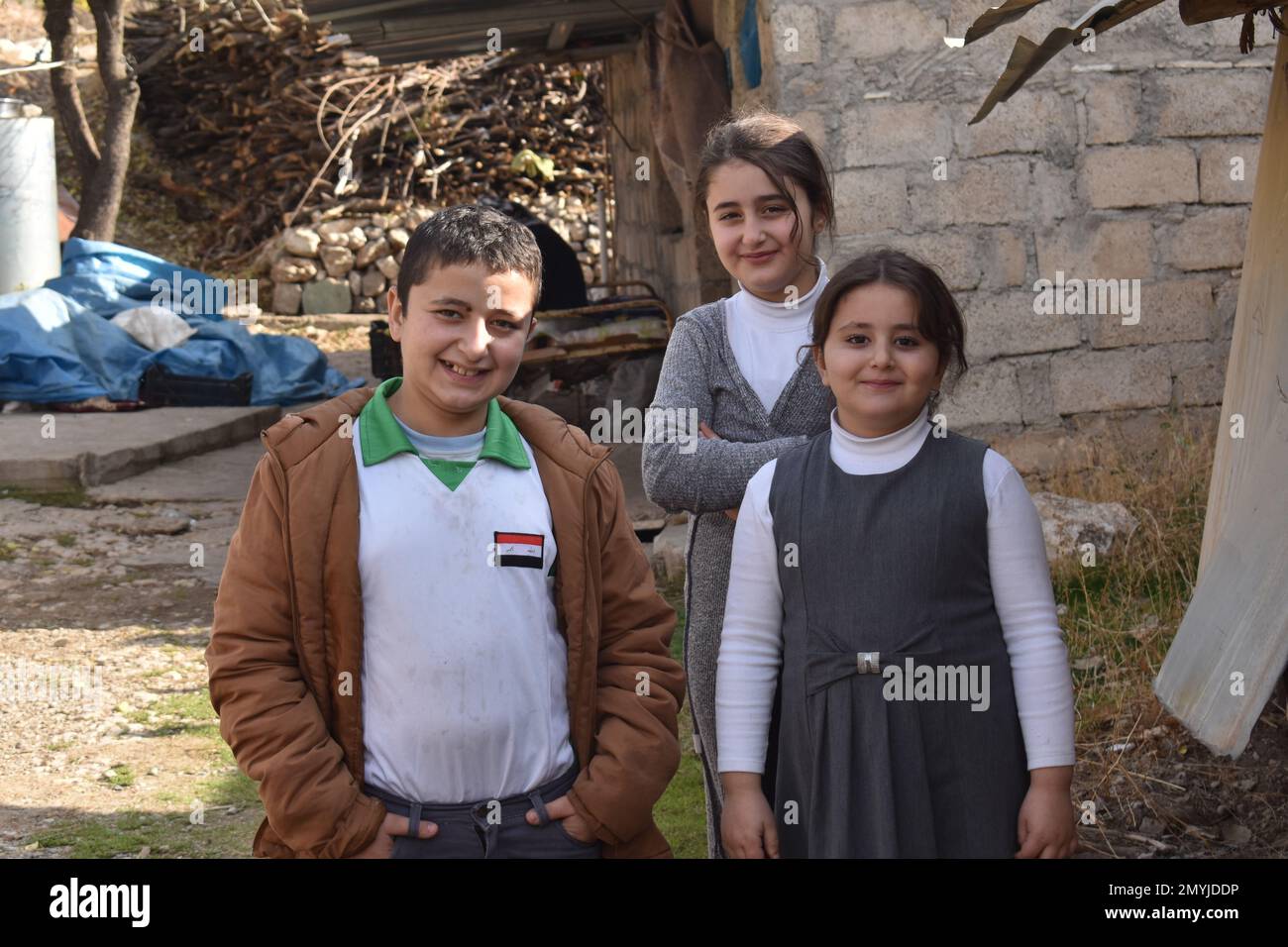 Drei Schulkinder stehen vor ihrer Familie in einem Dorf im Nordirak Stockfoto