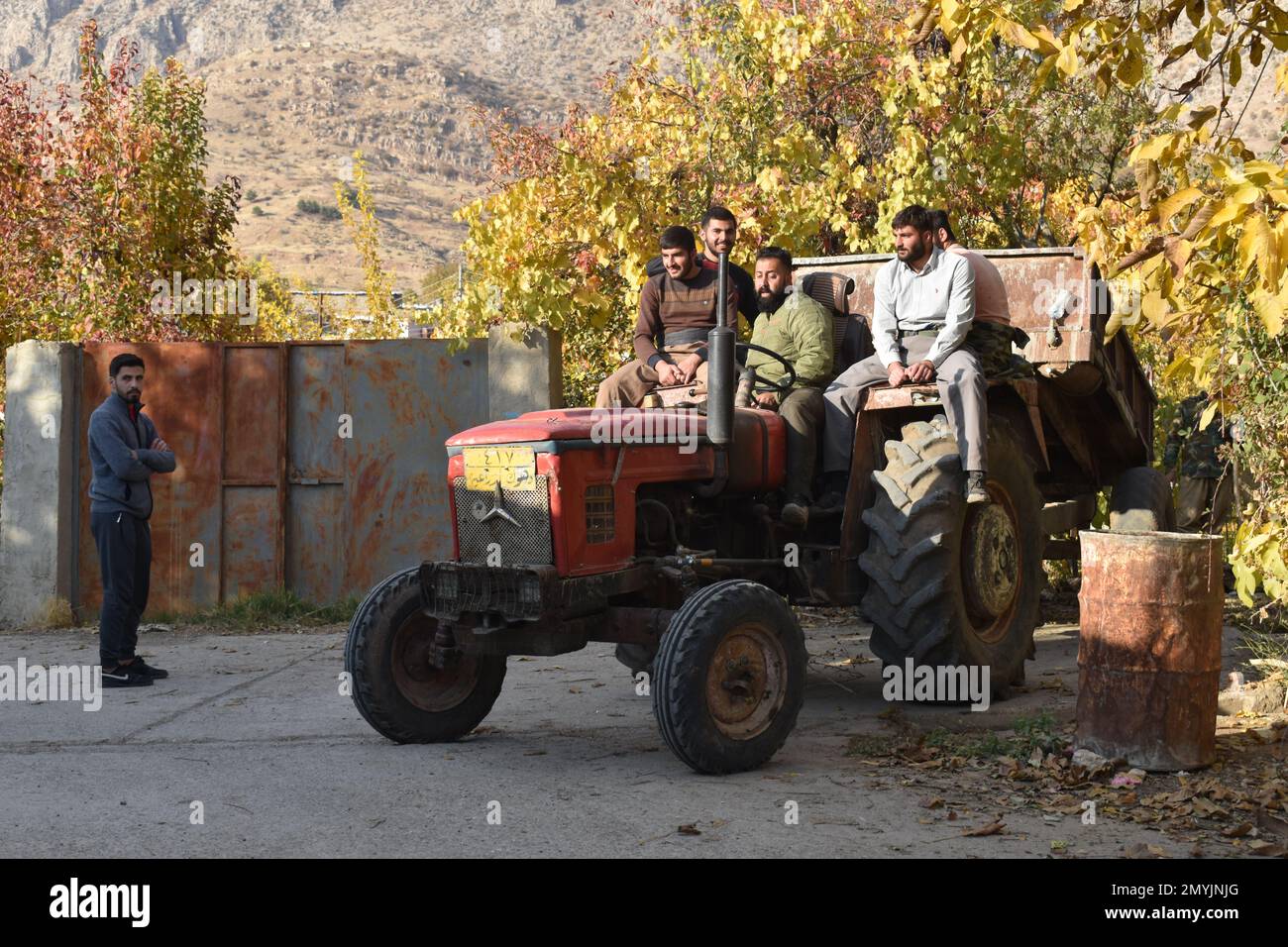 Fünf Männer fahren auf einem alten, roten Traktor in einem Dorf im Nordirak. Stockfoto