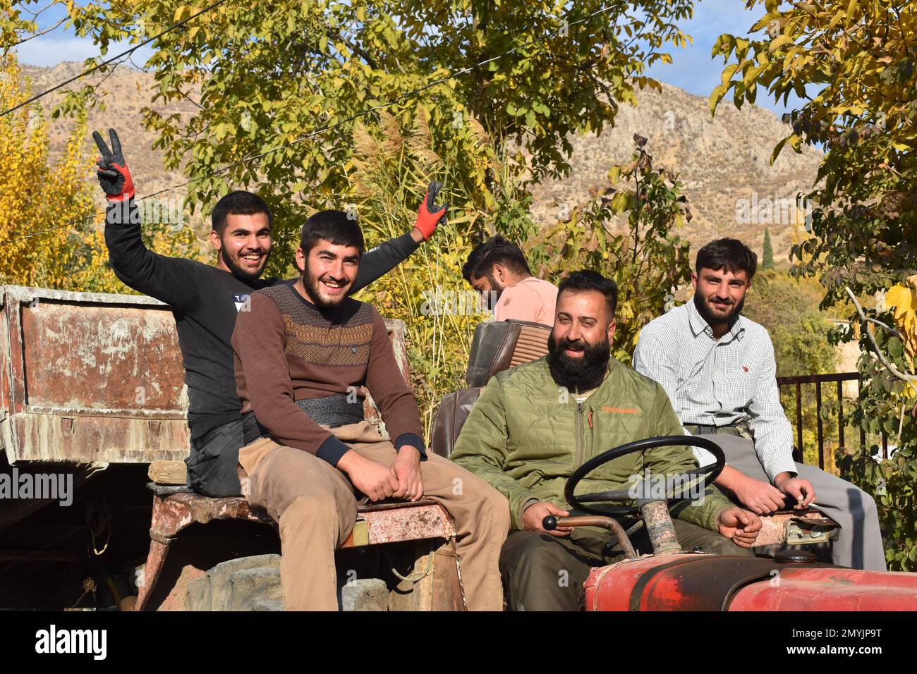Fünf lächelnde Männer fahren einen alten, roten Traktor in einem kurdischen irakischen Dorf Stockfoto