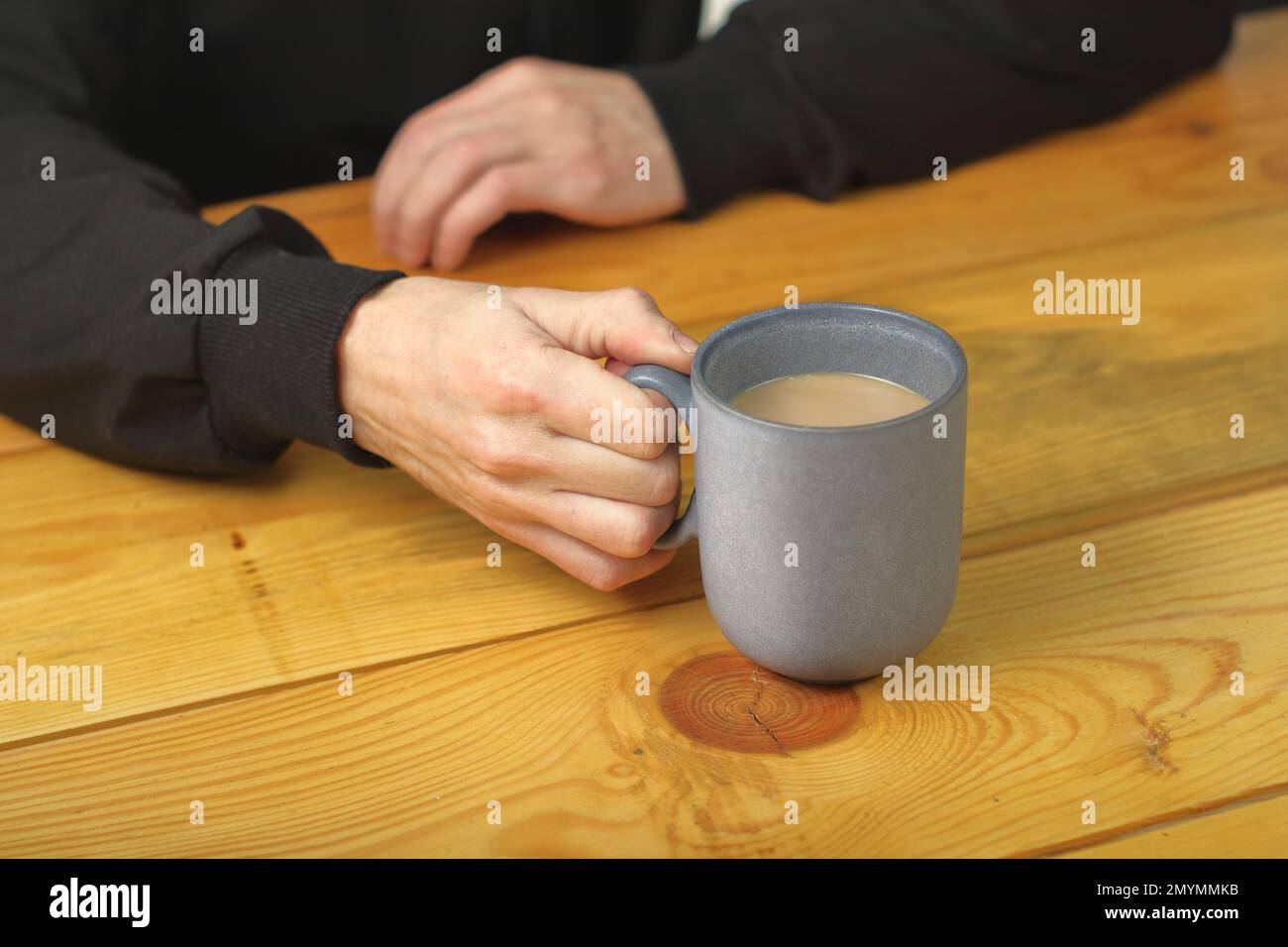 Person, die eine Tasse mit Kaffee auf einem Planktisch hält Stockfoto