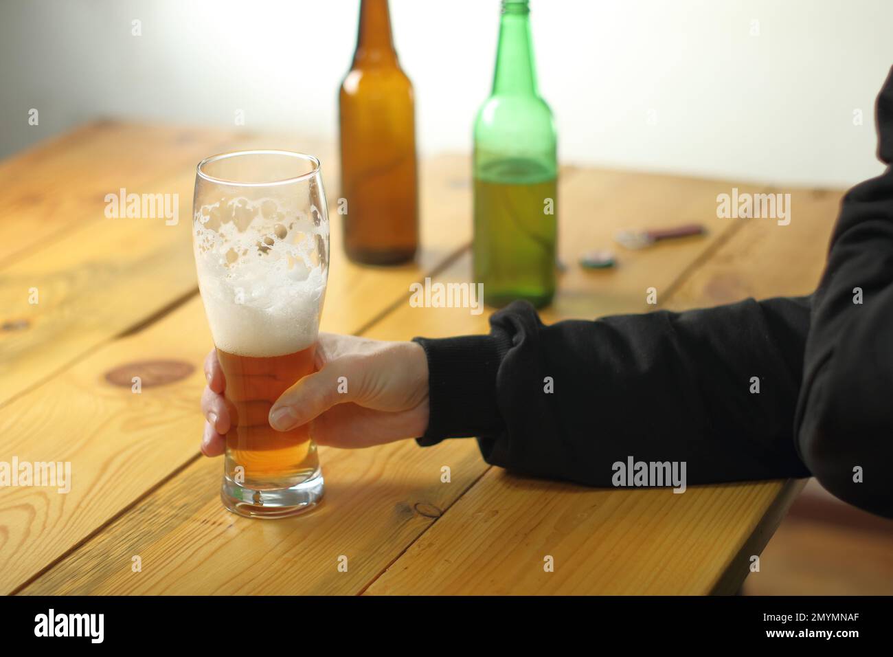 Die Person hält ein Pint mit halb vollem Bier auf dem Tisch und Hintergrund aus Flaschen Stockfoto