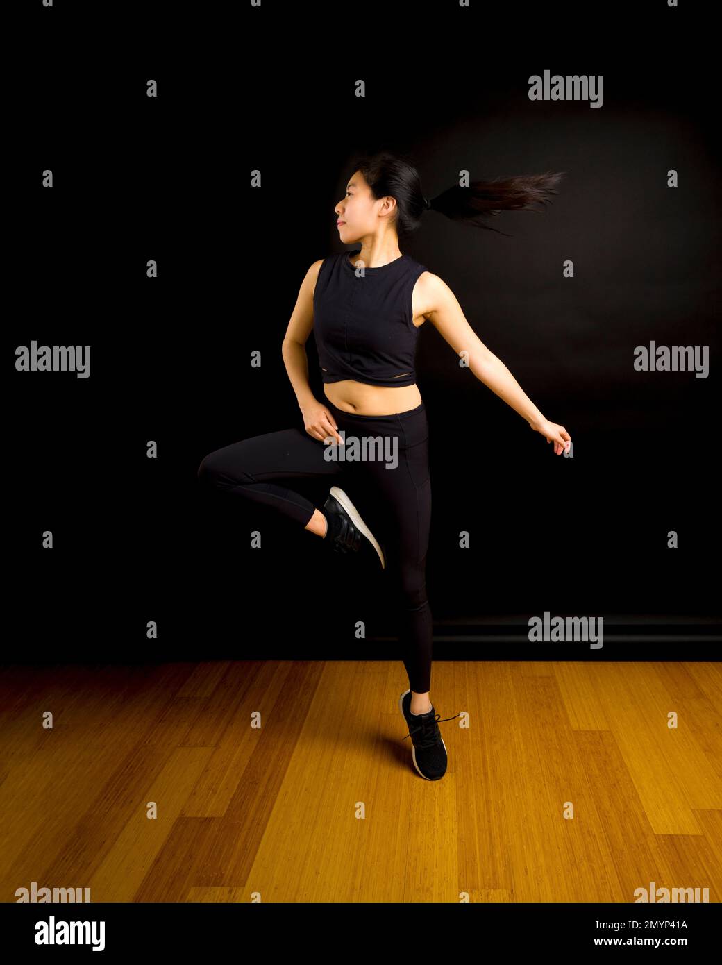 Fit Young Asian Dancer Woman Jumping and Spinning mit Pferdeschwanz im schwarzen Hintergrund Stockfoto