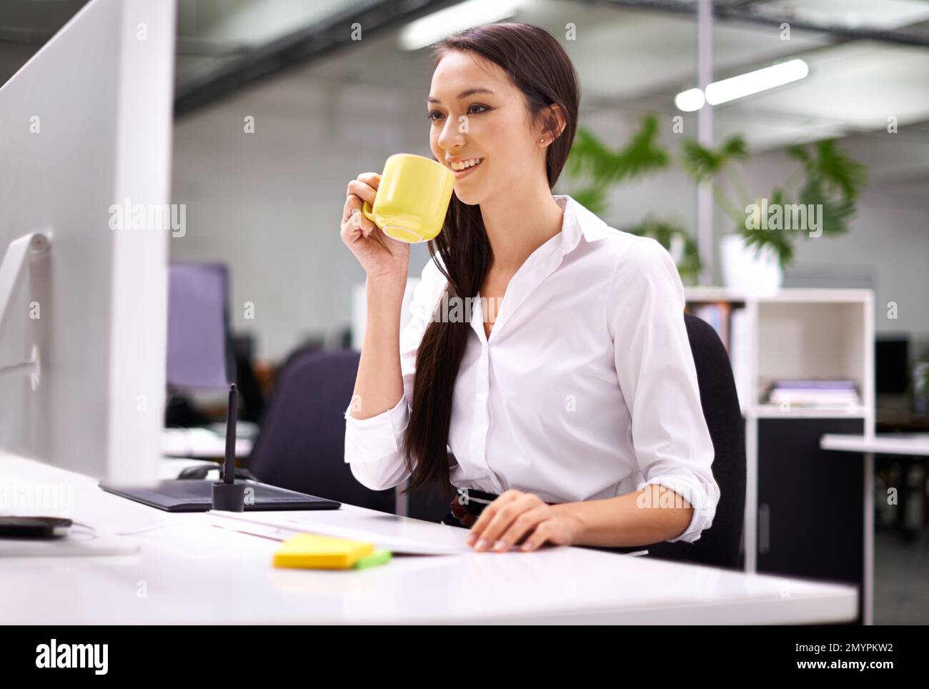 Beginnen Sie Ihren Arbeitstag mit einer Tasse Kaffee. Eine attraktive junge Frau, die an ihrem Schreibtisch arbeitet. Stockfoto