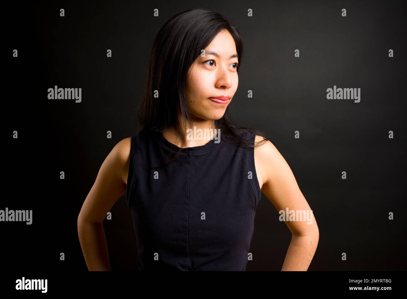 Profil der Athletic Young Asian Woman mit Händen an der Hüfte | Schwarzer Hintergrund | Trainingsbekleidung Stockfoto