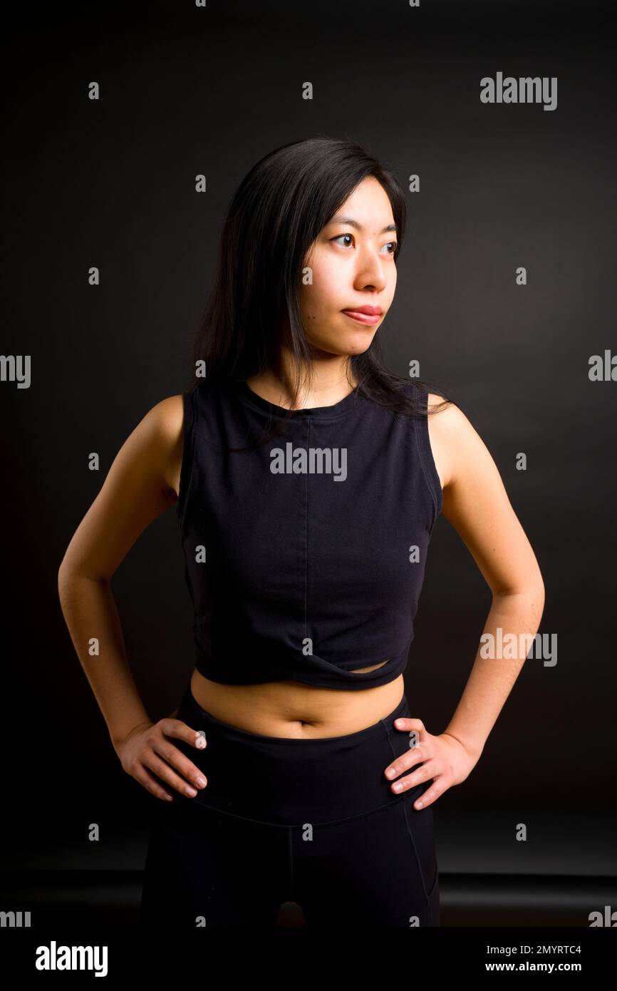 Profil der Athletic Young Asian Woman mit Händen an der Hüfte | Schwarzer Hintergrund | Trainingsbekleidung Stockfoto