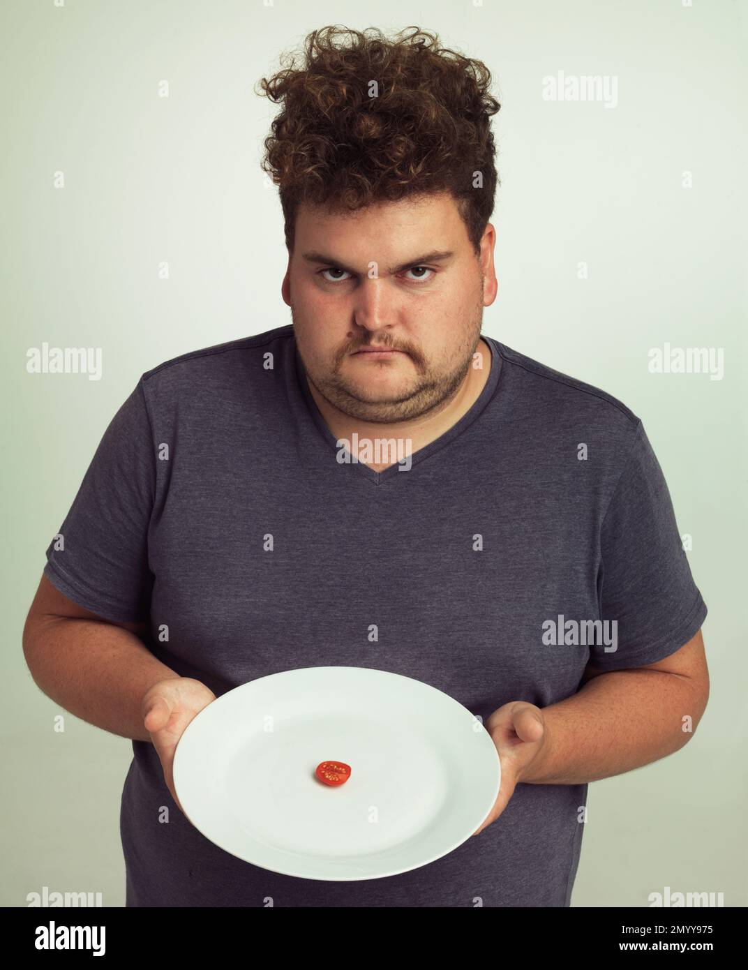 Wo ist der Rest meines Burgers? Porträt eines übergewichtigen Mannes, der einen Teller mit einem kleinen Stück Tomate hält. Stockfoto