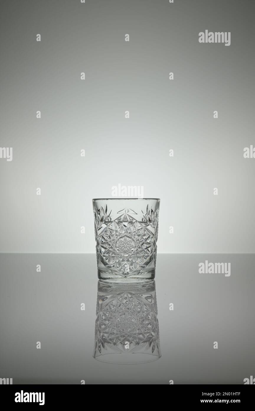 Ein kristallklares Wasserglas, das auf einer grauen Oberfläche mit weißem Hintergrund reflektiert wird Stockfoto