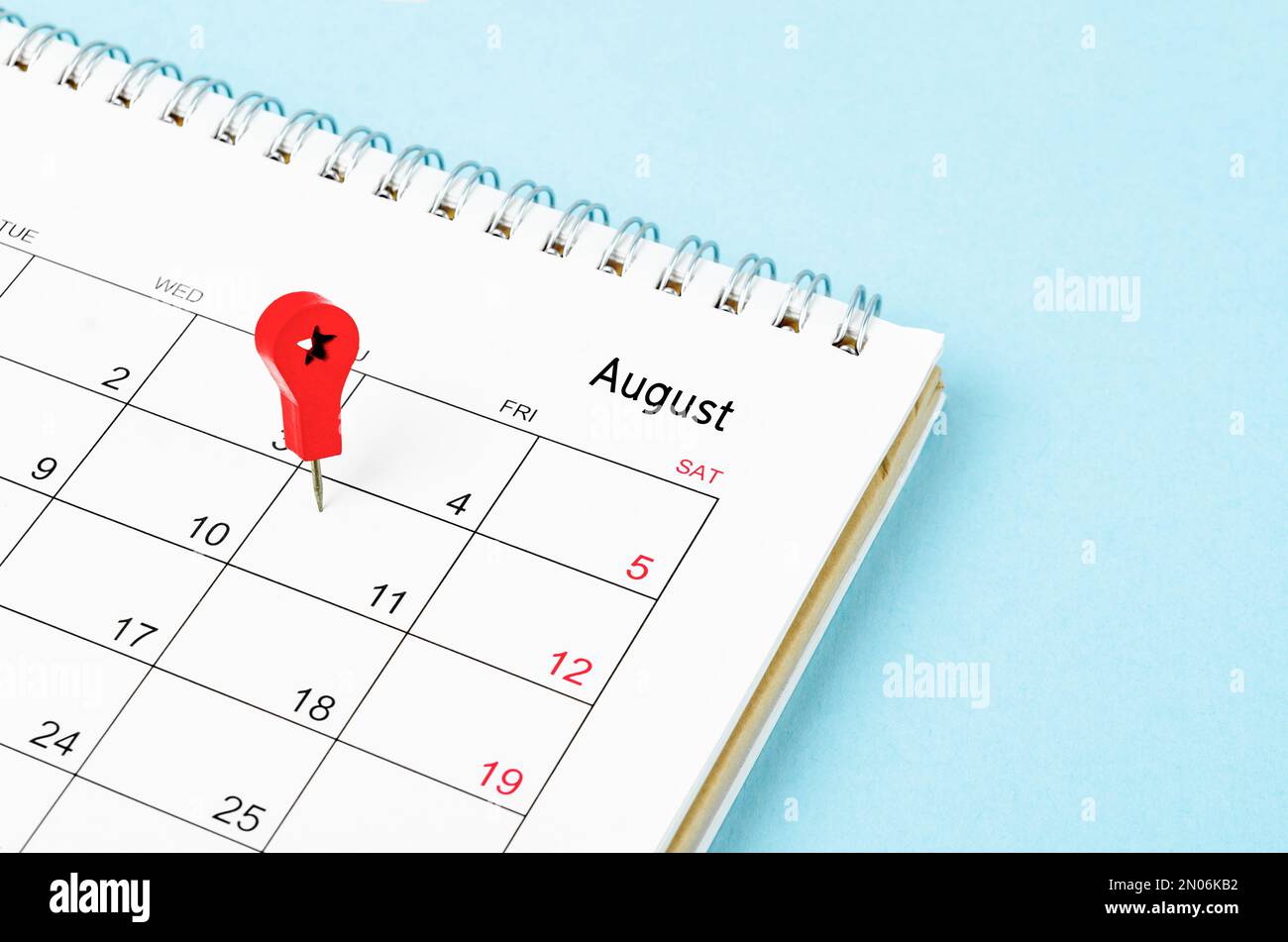 Gestickte Holznadeln auf einem leeren Kalender am Freitag, den 11. August, mit selektivem Fokus auf blauem Hintergrund. Stockfoto