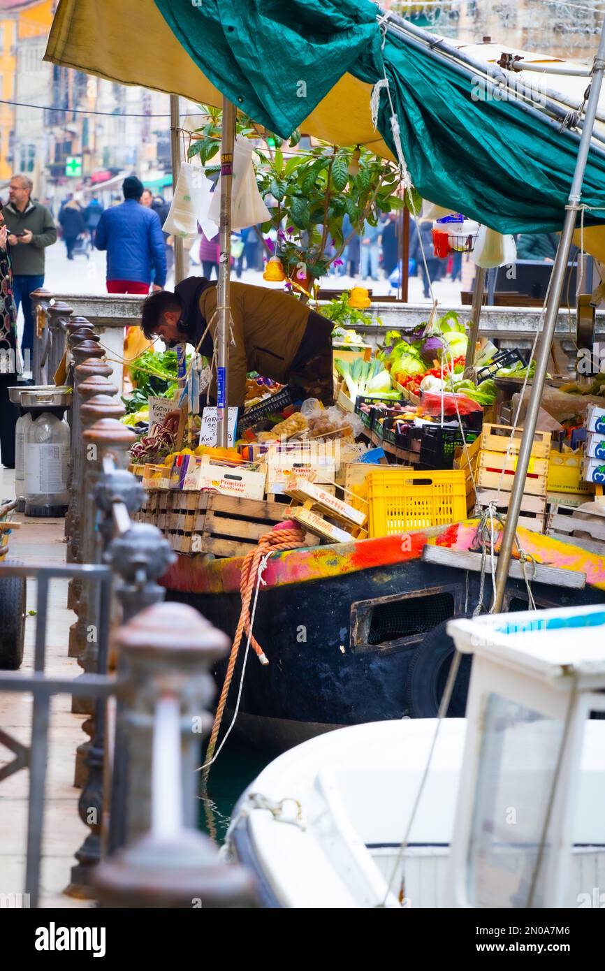 Ein Lebensmittelmarkt im Freien mit bunten Produkten und Touristen, die vorbeilaufen, vertikal Stockfoto