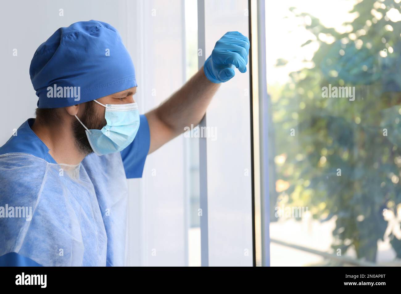 Gestresster Arzt in der Nähe von Fenstern im Haus. Psychischer Druck von Beschäftigten im Gesundheitswesen während der COVID-19-Pandemie Stockfoto