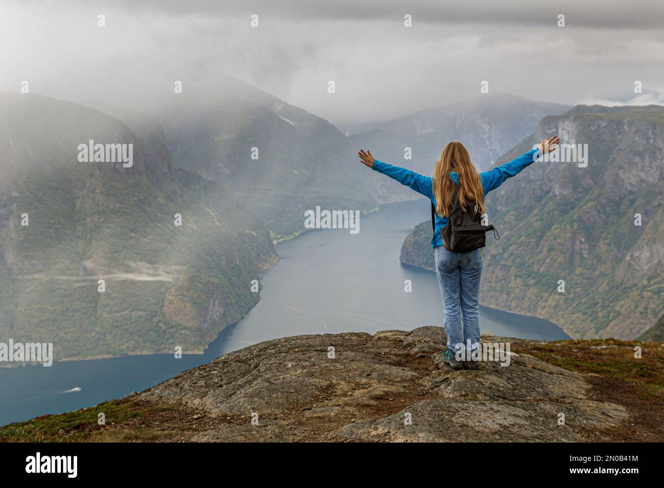 Ein Mädchen steht auf einem Berg über dem Aurlandsfjord in Norwegen und reckt die Hände in die Höhe, Norwegen Europa. Stockfoto