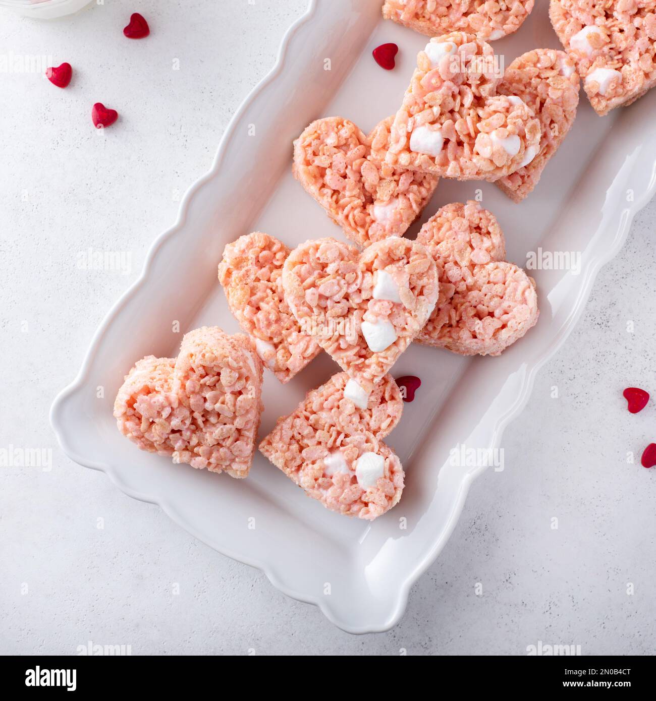Herzförmige rosafarbene Reiskrispie zum Valentinstag auf einem Teller mit roten Herzstreuseln Stockfoto
