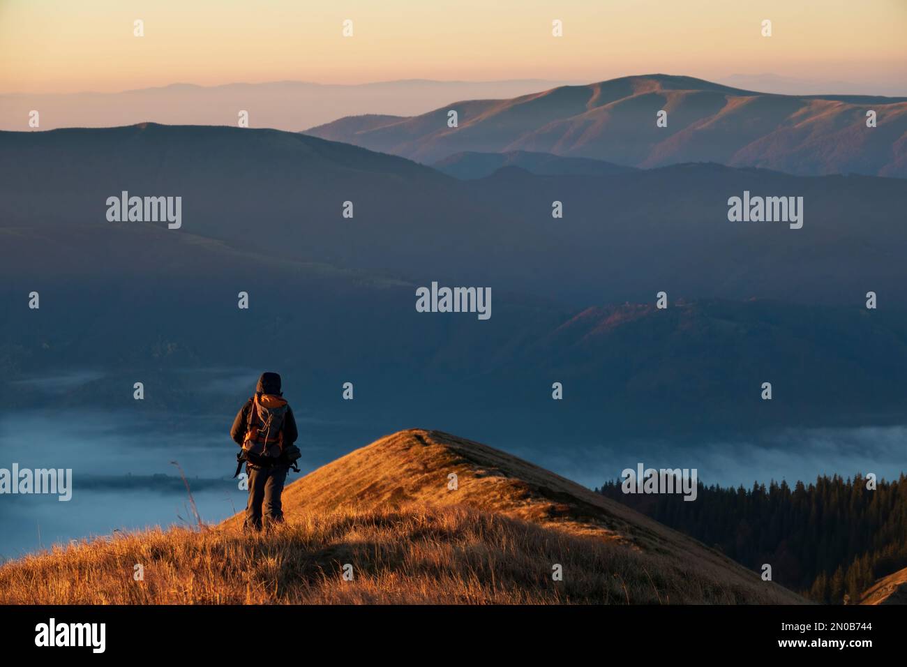 Einsamer Mann, der bei Sonnenuntergang auf dem Gipfel des Berges spaziert. Reisen, Erkunden und Wanderlust-Konzept Stockfoto