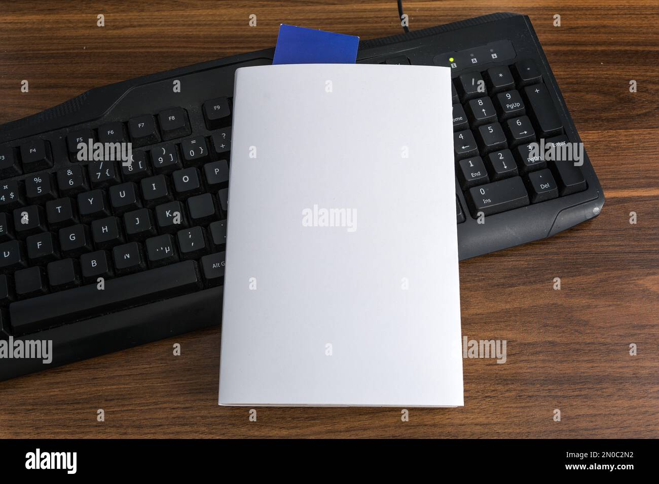 Leere weiße Buchumschlagsvorlage mit blauem Lesezeichen auf der schwarzen Tastatur. Beschneidungspfad. Stockfoto