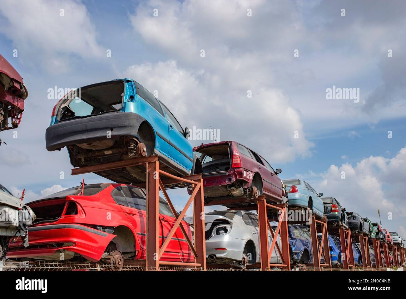 Gestapelte Autos auf einem Metallrahmen, der für Teile verwendet wird. Scrapyard-Perspektive mit blauem Himmel und flauschigen Wolken. Viel Speicherplatz für Kopien Stockfoto