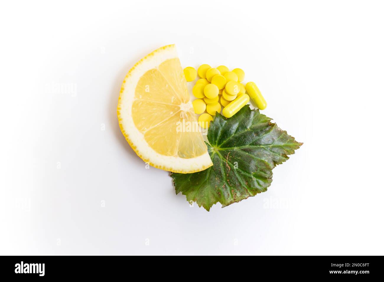 Eine halbe Zitronenscheibe neben gelben Pillen und Kapseln und ein grünes Blatt isoliert auf weißem Hintergrund Stockfoto