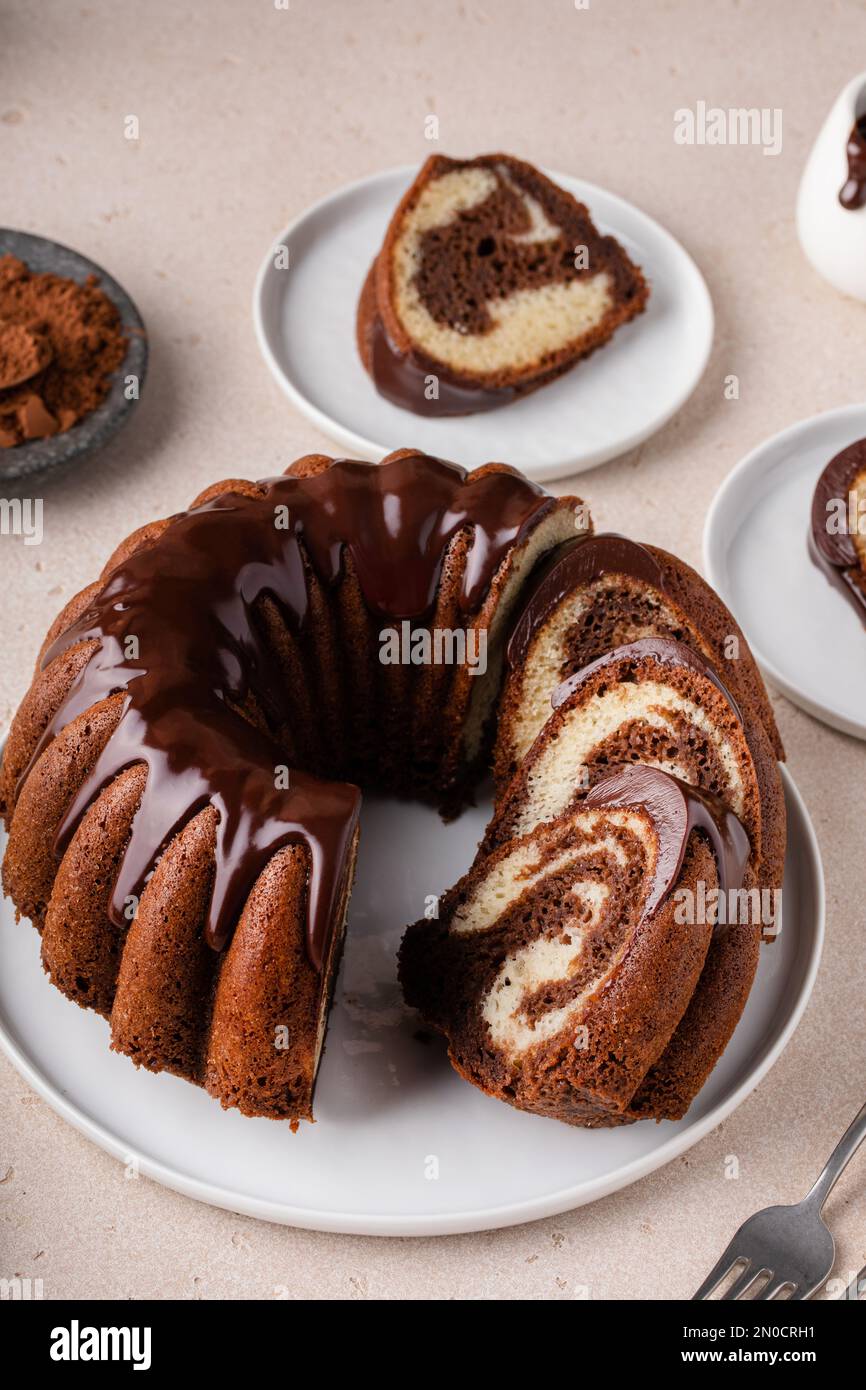 Schokoladenkuchen aus Marmor oder Zebrakuchen mit Schokoladenglasur, die auf einem Teller gestreut wird Stockfoto