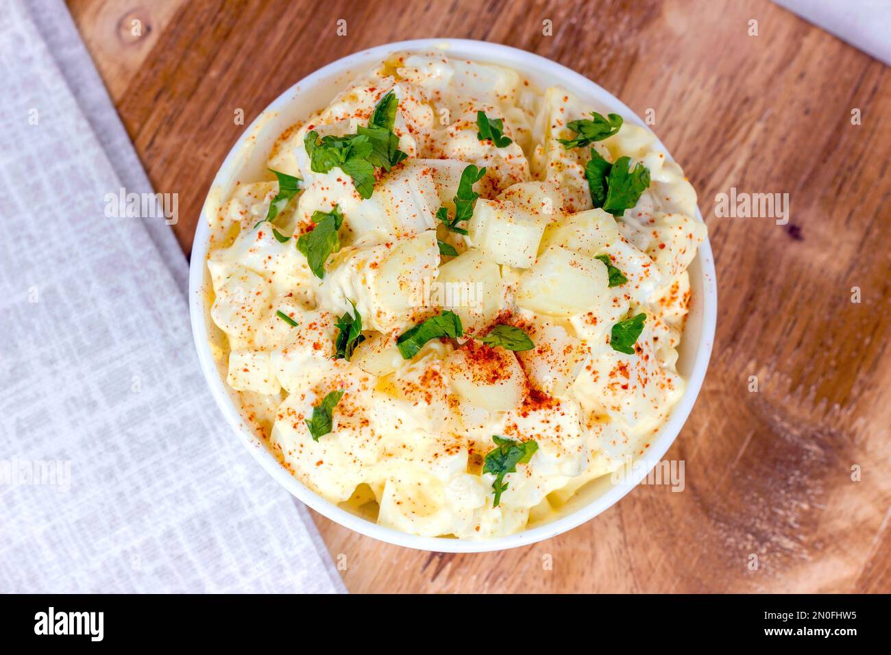 Frischer, hausgemachter traditioneller Amish-Kartoffelsalat mit Kartoffeln, gekochten Eiern, cremigem Dressing und Sellerie in einer weißen Schüssel auf Holzhintergrund Stockfoto