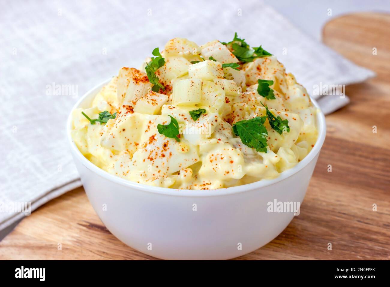 Frischer, hausgemachter traditioneller Amish-Kartoffelsalat mit Kartoffeln, gekochten Eiern, cremigem Dressing und Sellerie in einer weißen Schüssel auf Holzhintergrund Stockfoto