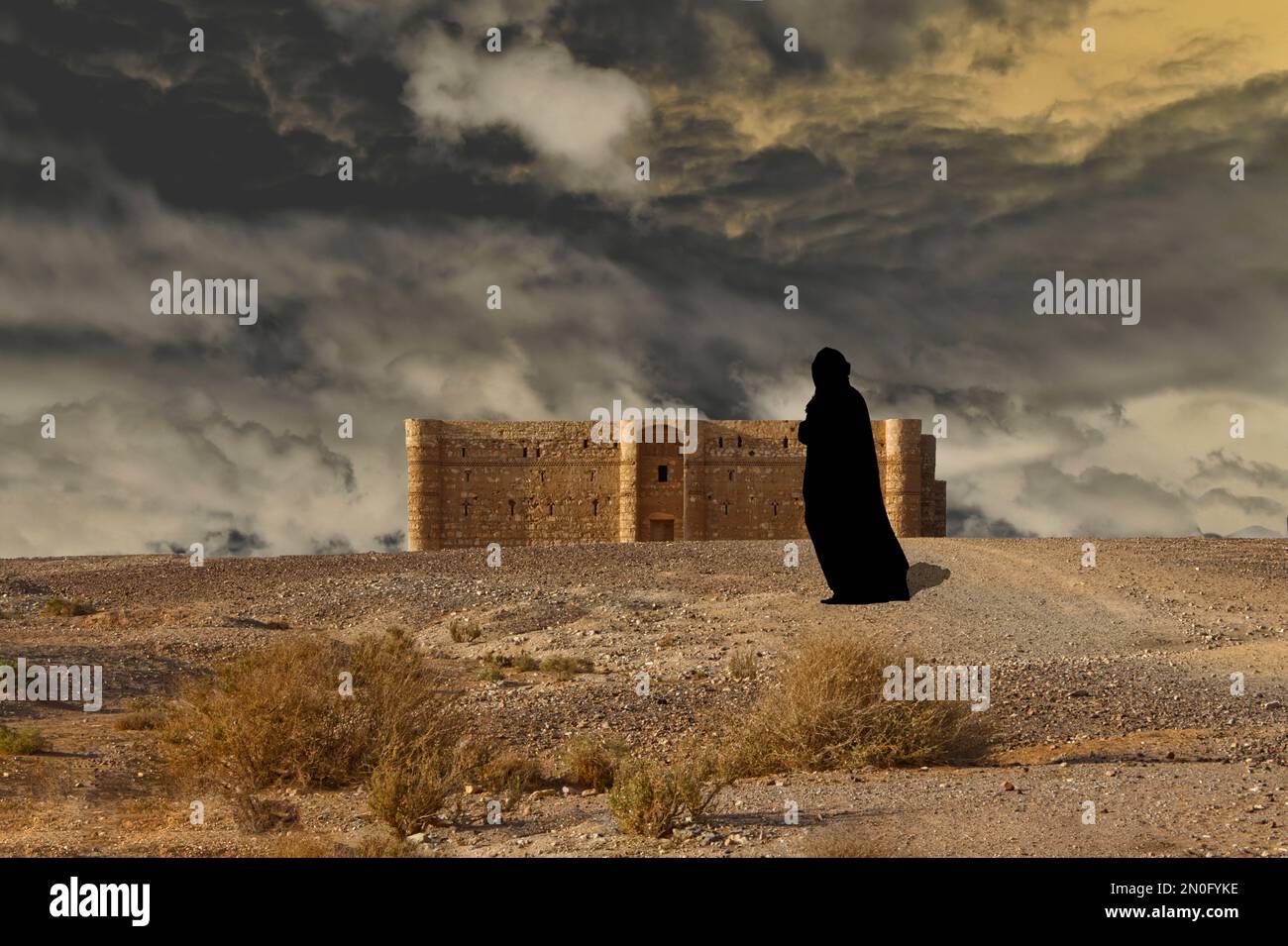 Araberin in Schwarz gegen das alte Schloss und das bewölkte Wetter in der Wüste Stockfoto