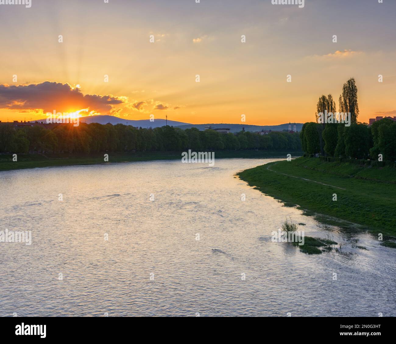 Herrlicher Sonnenaufgang am Ufer des Flusses uzh. Wunderschöne Stadtlandschaft im Zentrum von uschhorod im Frühling. Grasböcke der längsten Lindenallee in der Gegend Stockfoto