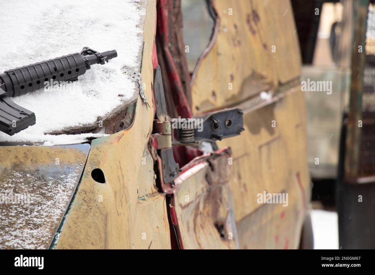 Eine Kinderpistole aus Plastik liegt auf einem Militärfahrzeug, das im Winter, dem Krieg in der Ukraine, auf der Straße in der Ukraine zerstört wurde Stockfoto