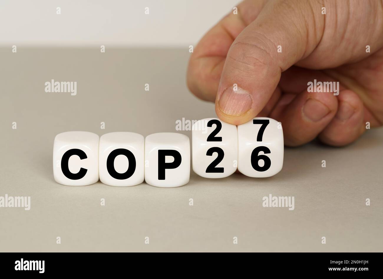 Auf einer grauen Oberfläche befinden sich weiße Würfel mit der Aufschrift COP26 bis COP27. Zwei Würfel in der Hand. Technologiekonzept Stockfoto