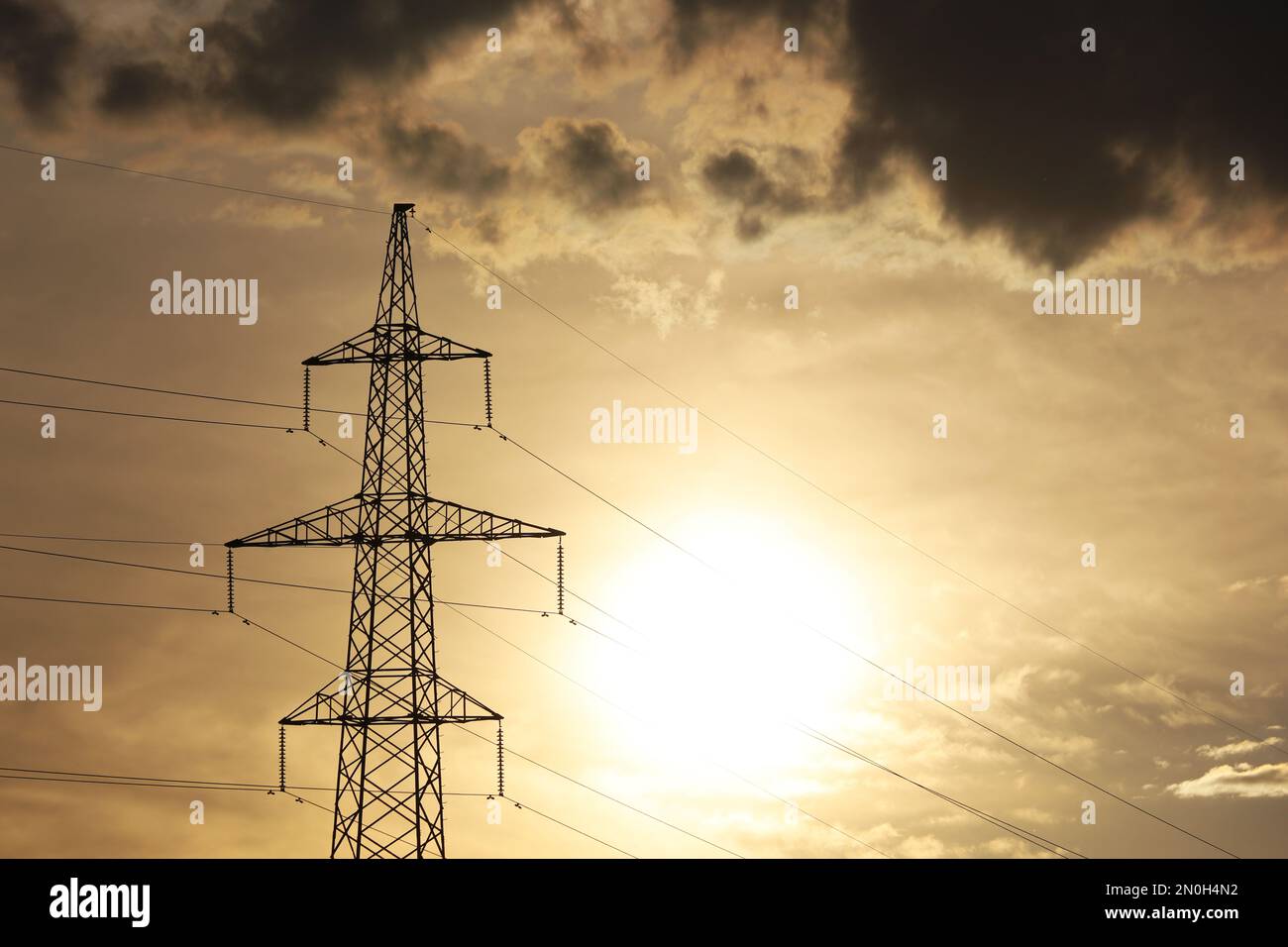 Silhouette eines Hochspannungsturms mit elektrischen Drähten auf dem Hintergrund des Sonnenuntergangs und dunkler Wolken. Stromübertragungsleitungen, Stromversorgung Stockfoto