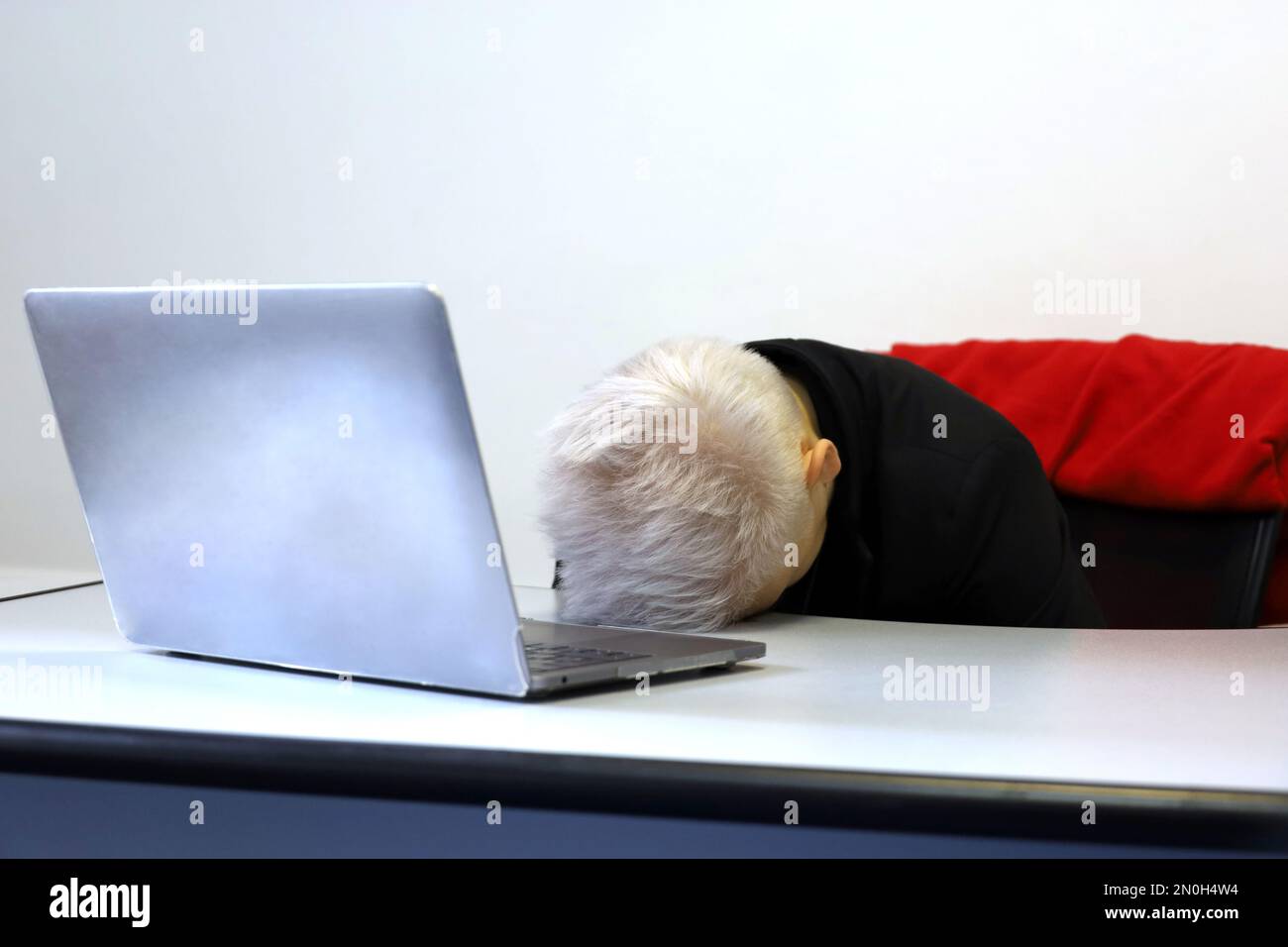 Ein Mädchen mit kurzen gefärbten Haaren, das neben dem Laptop am Bürotisch schläft. Konzept von überarbeitetem Mitarbeiter, müde nach der Arbeit, schlaflose Nacht Stockfoto