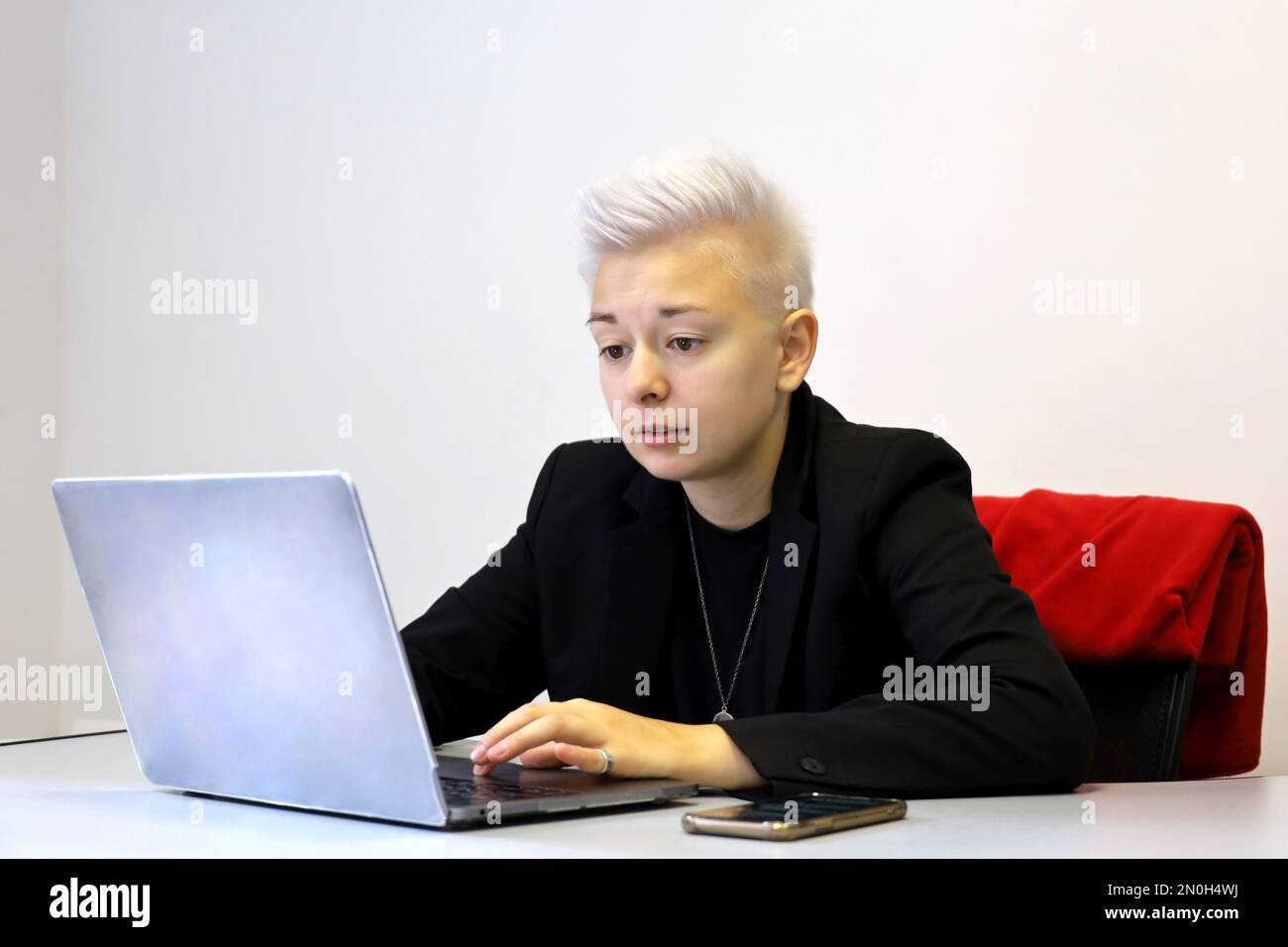 Mädchen mit kurzen blonden Haaren, die am Laptop sitzen, mit besorgtem Gesichtsausdruck am Schreibtisch. Tomboy Lifestyle, Konzept der schwierigen Aufgabe Stockfoto