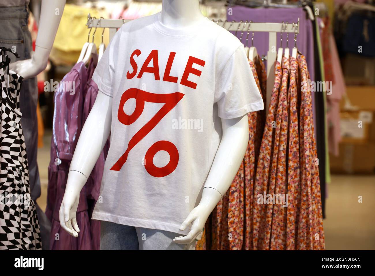 T-Shirt mit Sale-Inschrift im Bekleidungsgeschäft. Verschiedene Kleidung für Männer und Frauen auf einem Gestell Stockfoto