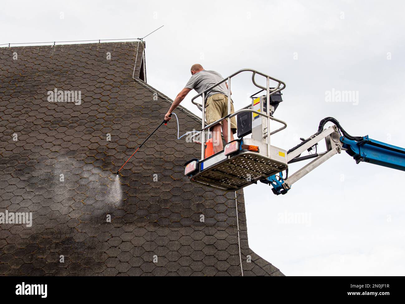 Ein Hausbesitzer, der im Sommer im Freien Moos auf ein Hausdach spritzt und Chemikalien entfernt. Moosentfernungskonzept. Stockfoto