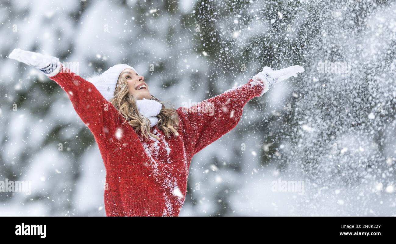 Mit weit geöffneten Armen genießt Frau in rotem Pullover, weißen Handschuhen, Schal und Hut an einem verschneiten Wintertag frische Luft. Stockfoto