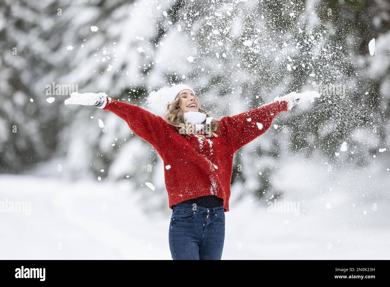 Mit weit geöffneten Armen genießt Frau in rotem Pullover, weißen Handschuhen, Schal und Hut an einem verschneiten Wintertag frische Luft. Stockfoto