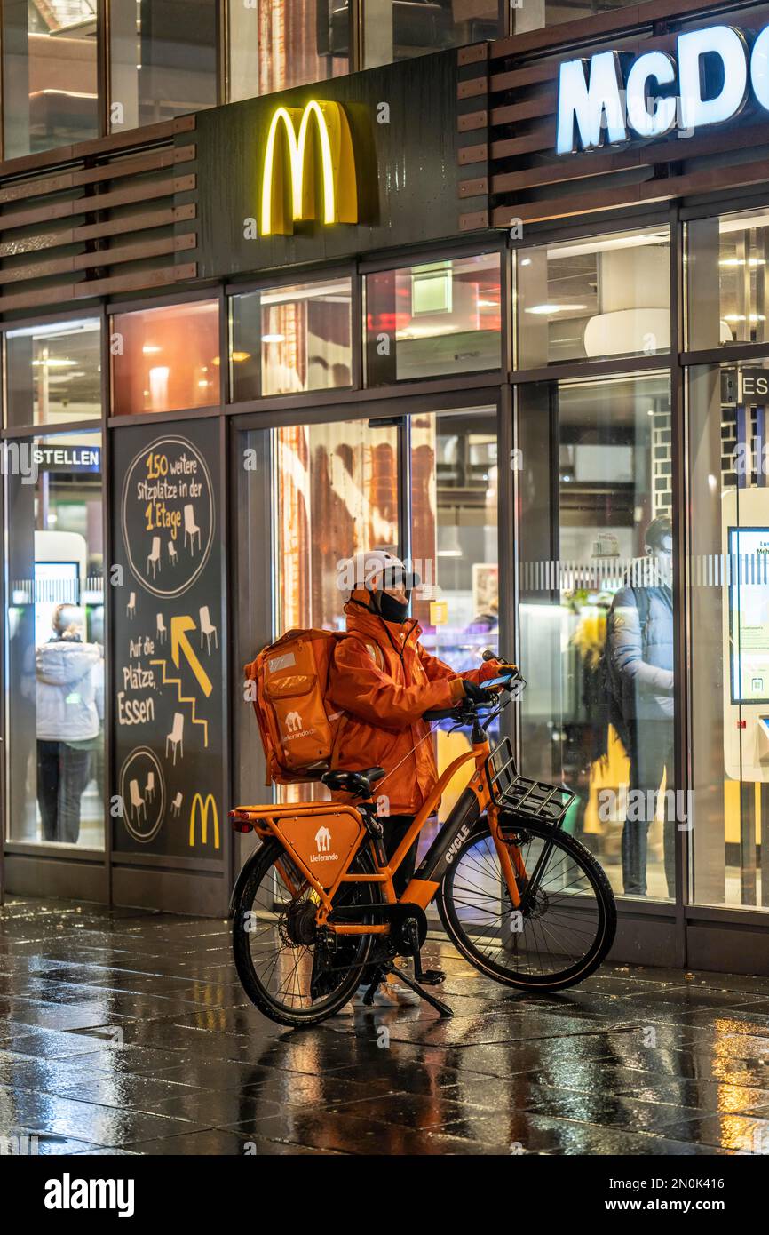 Straße am Hauptbahnhof, Lieferando Kurier, Radfahrer, Regenwetter, Stadtzentrum, Am Abend essen, NRW, Deutschland, Stockfoto