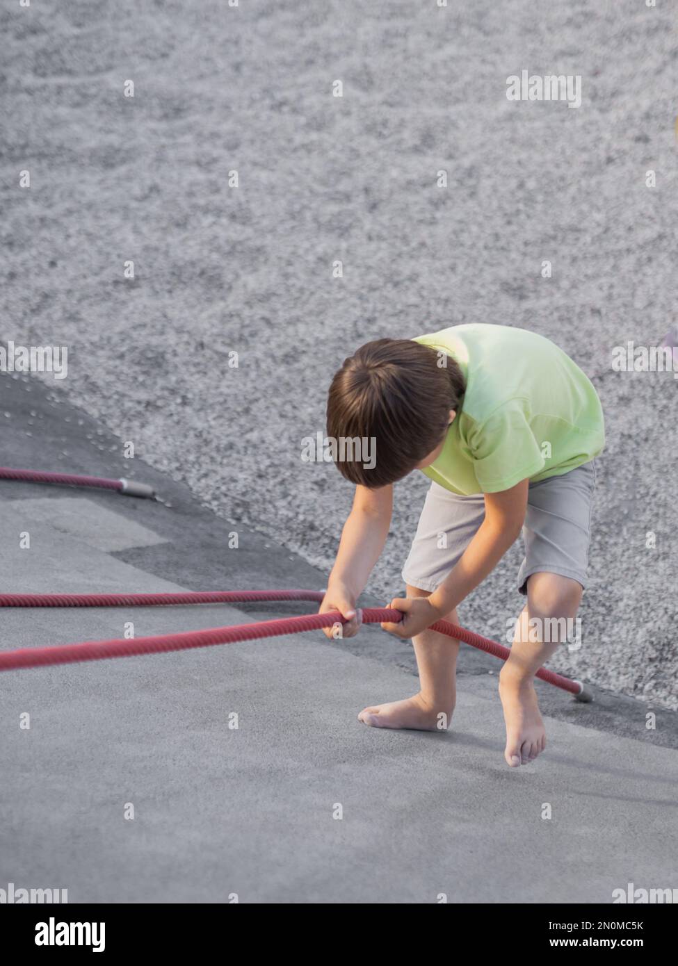 Der Junge klettert einen Betonhang auf dem modernen Kindersport- und Spielplatz hinauf. Das Kind überwindet die Angst und lernt neue Dinge. Aktive Freizeitaktivitäten im Freien. Stockfoto