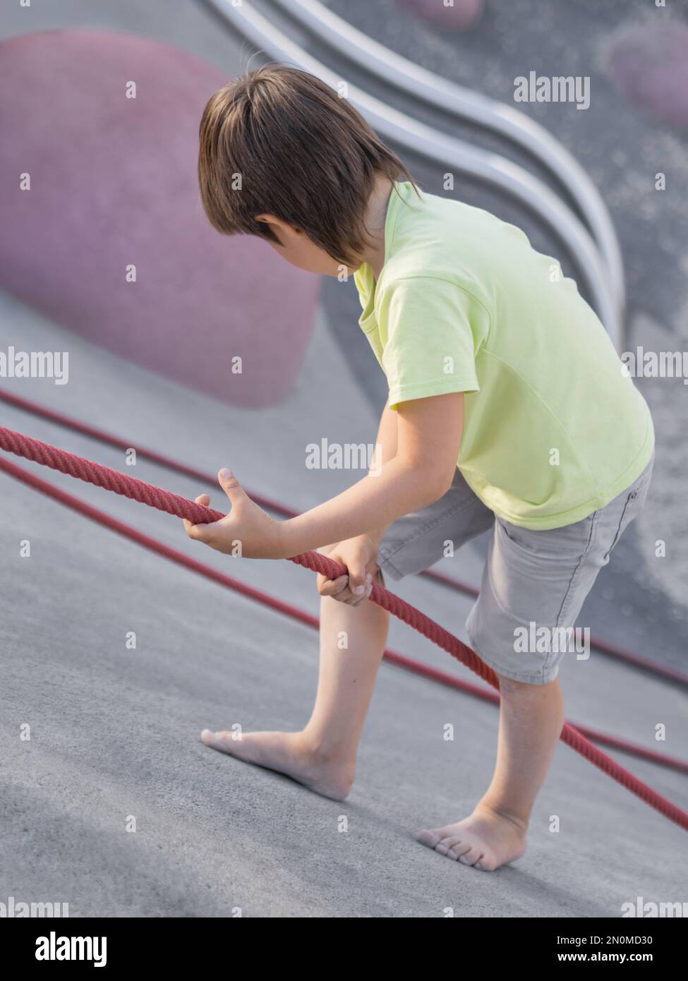 Der Junge klettert einen Betonhang auf dem modernen Kindersport- und Spielplatz hinauf. Das Kind überwindet die Angst und lernt neue Dinge. Aktive Freizeitaktivitäten im Freien. Stockfoto