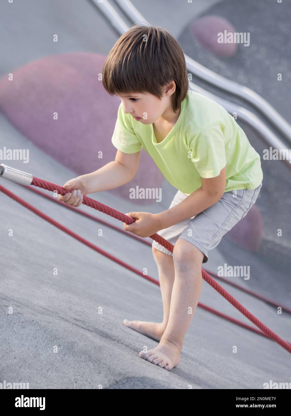 Der Junge klettert einen Betonhang auf dem modernen Kindersport- und Spielplatz hinauf. Das Kind überwindet die Angst und lernt neue Dinge. Aktive Freizeitaktivitäten im Freien. Stockfoto