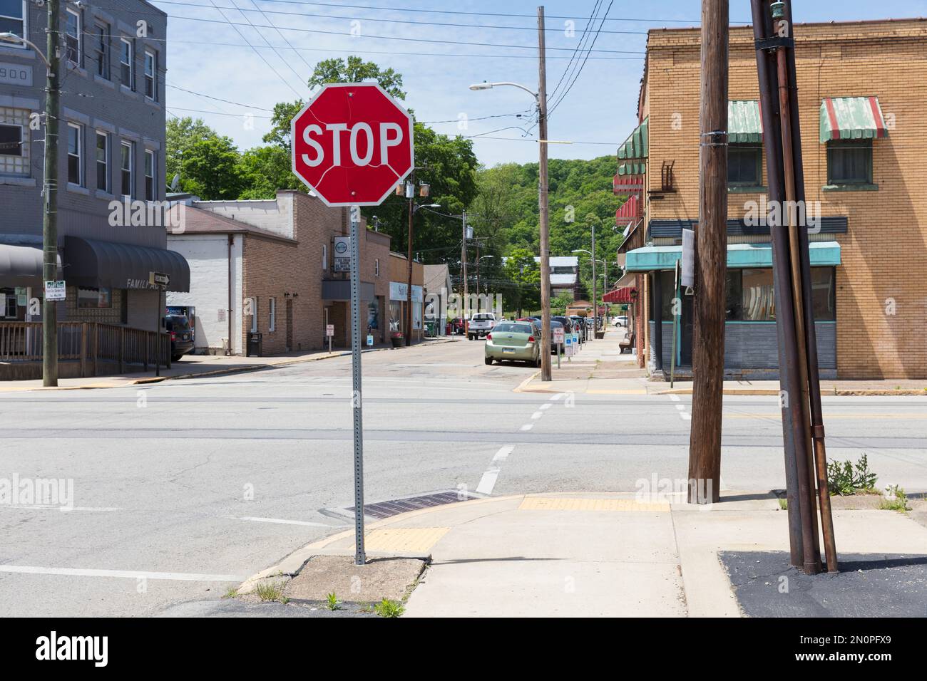 Ein Stoppschild und ein Fußgängerüberweg in einer kleinen Stadt, und Sie haben einen Blick auf eine Straße mit Geschäften und geparkten Autos. Stockfoto