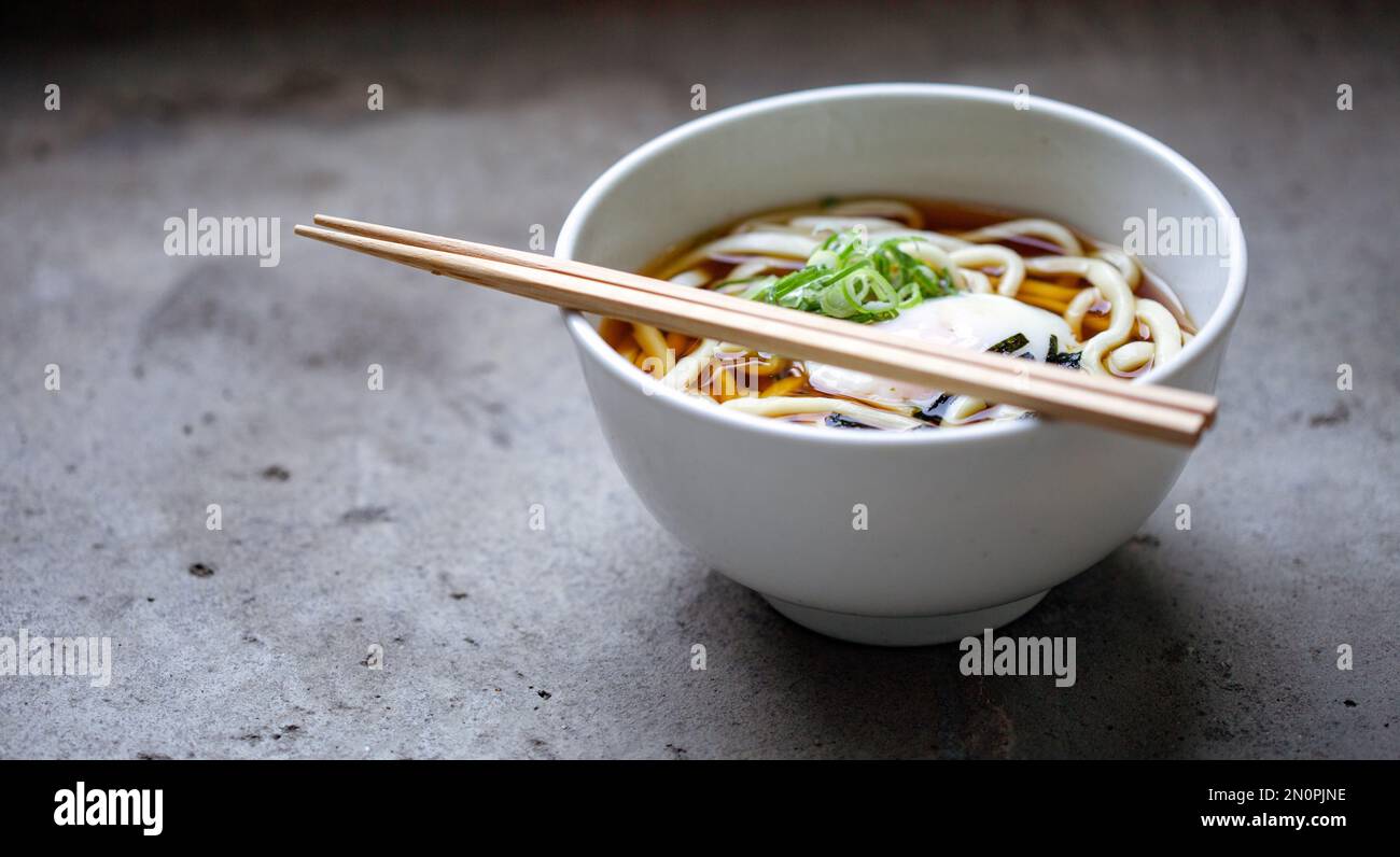 Eine Schüssel Nudeln, Gemüse und Brühe und ein Set Essstäbchen. Stockfoto