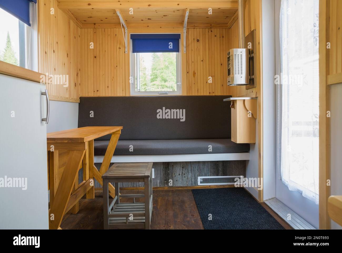 Weißer Melamin-Küchenschrank und erweiterbarer Pinienholz-Esstisch mit Bank im Hauptsitzbereich im 8 x 24 Fuß großen mobilen Minihaus. Stockfoto