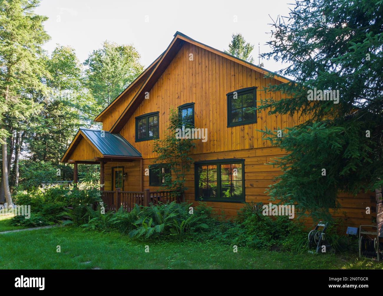 Gefräste Cottage Stil flache Holzprofil Haus Fassade mit Veranda und Landschaftsgestaltung im Sommer. Stockfoto