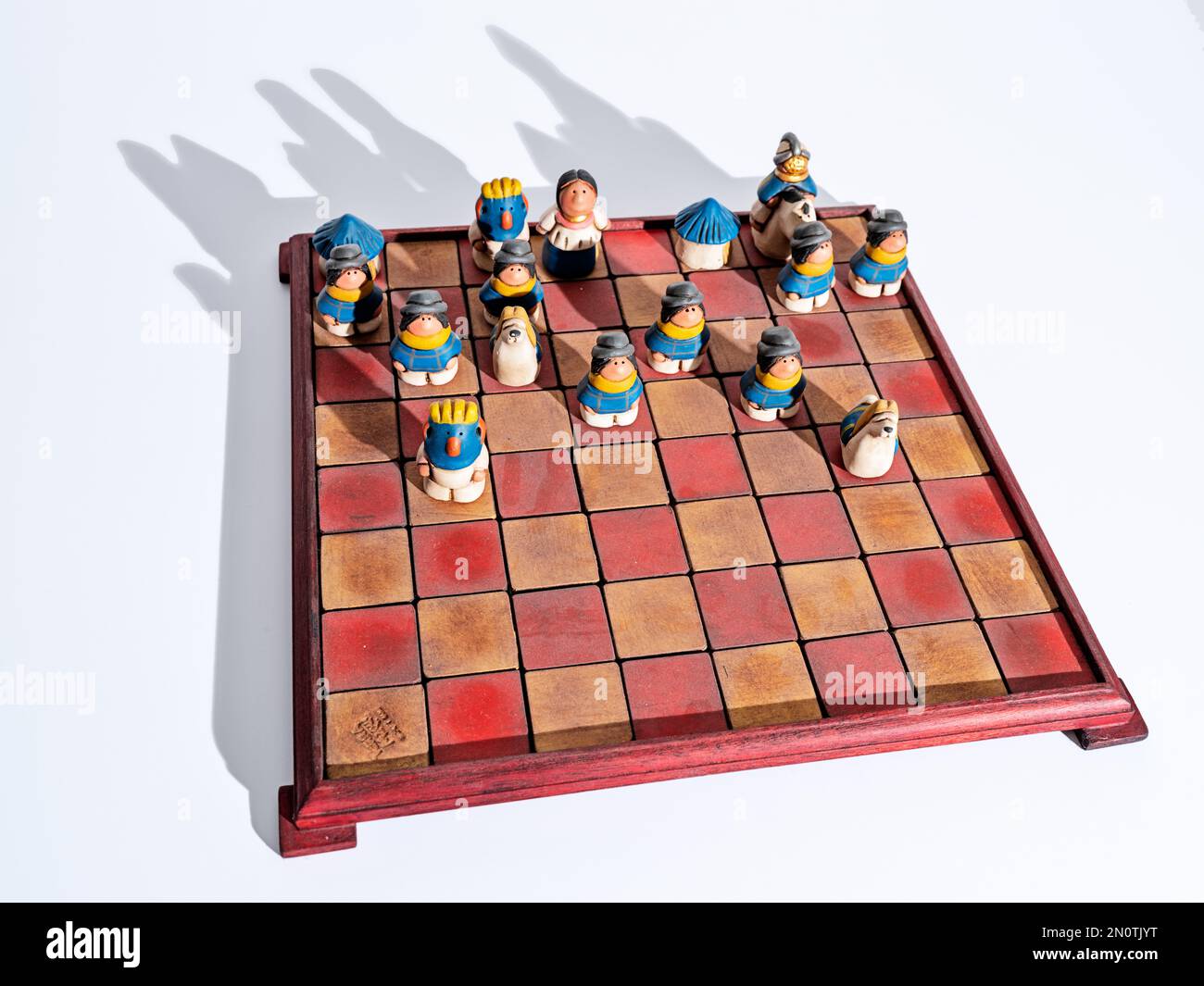 Ein handgemachtes Schachset aus Ecuador mit bunten Stücken auf dem Spielbrett mit weißem Hintergrund. Stockfoto