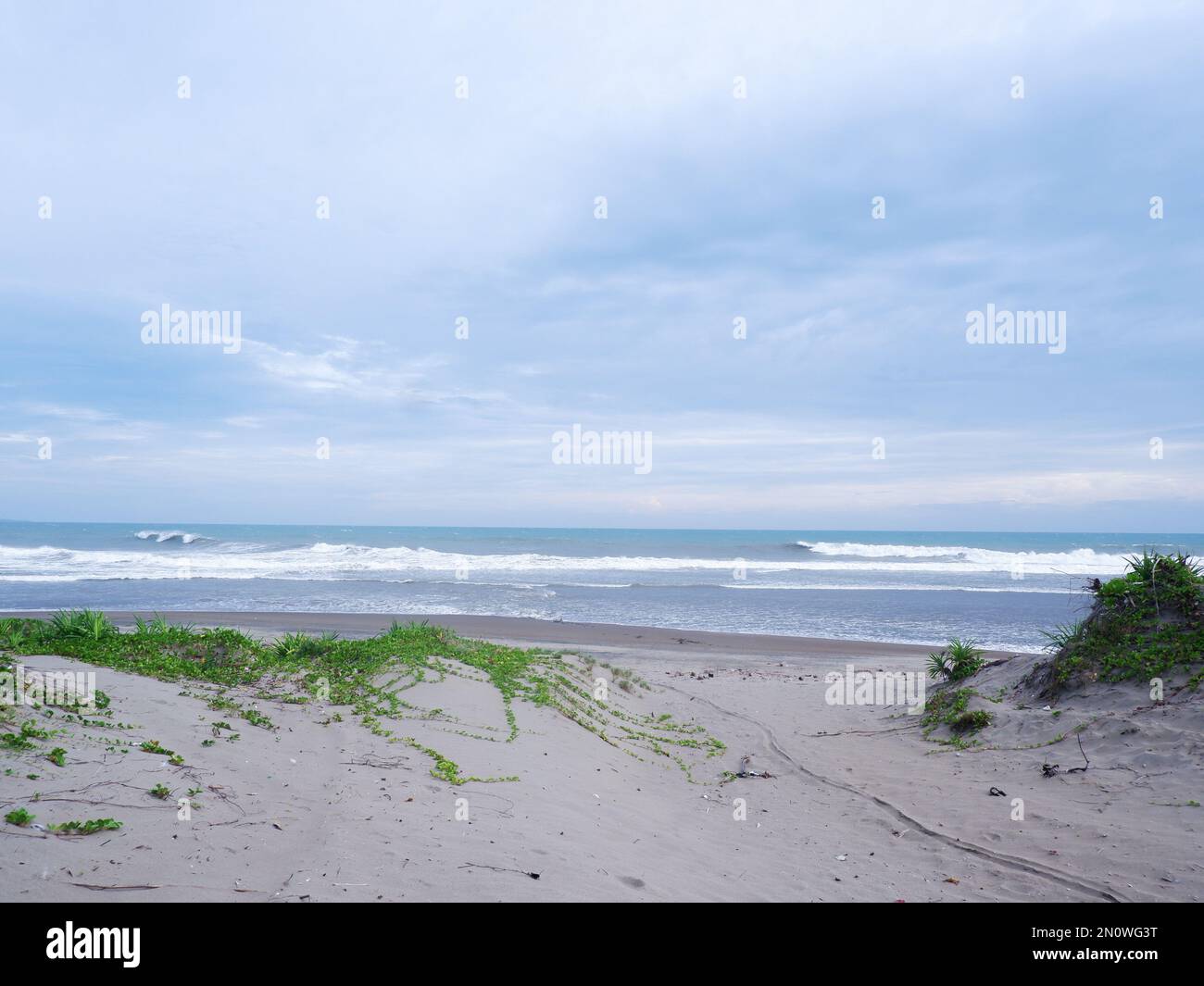 Türkisfarbenes Wasser, weiße Wellen, blauer Himmel, grünes Gras, weißer Sand, Wunderschöner Strand und wunderschöne Insel, Sayang Heulang Garut, Panoramablick Stockfoto