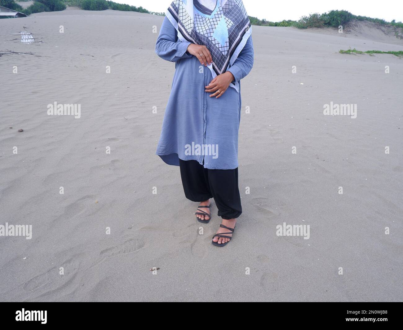 Der halbe Körper der Frau in Blau stand auf dem Strand Sand und faltete dann ihre Arme auf ihren Bauch Stockfoto