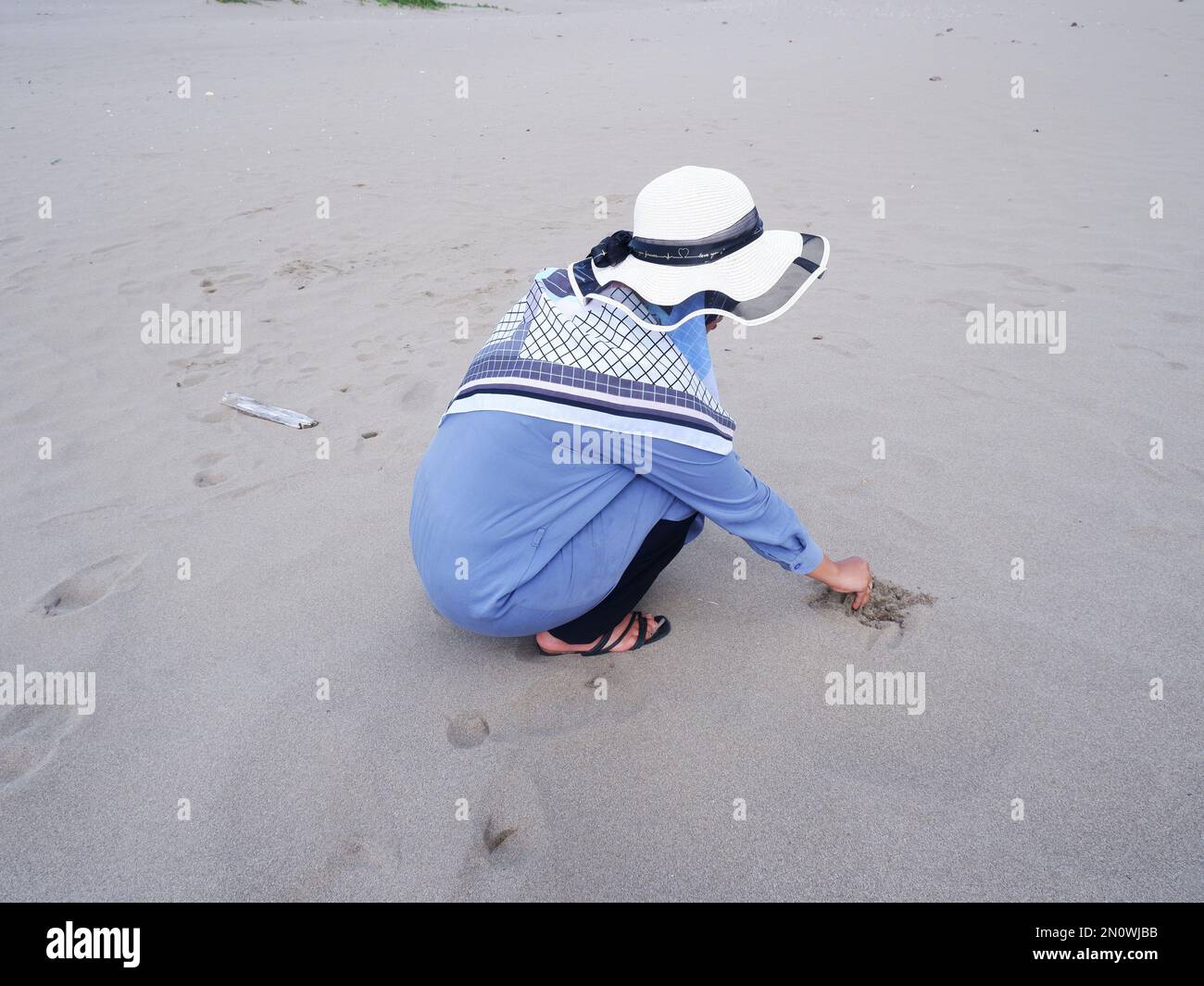 Der Rücken der Frau mit dem Hut am tropischen Strand, die auf dem Sandstrand saß und auf das Meer starrte, entstand dann Liebe aus der Hand. Rückgrat Stockfoto