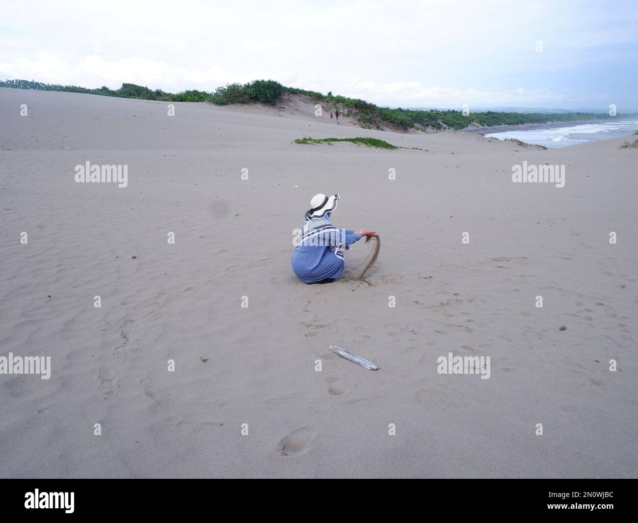 Der Rücken der Frau mit dem Hut am tropischen Strand, die auf dem Sandstrand saß und auf das Meer starrte, entstand dann Liebe aus der Hand. Rückgrat Stockfoto